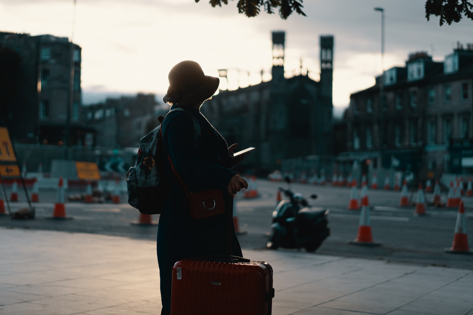 woman wearing coat standing on road with travel luggage during daytime