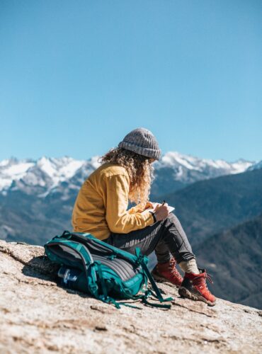 woman writing while sitting on hill near mountain