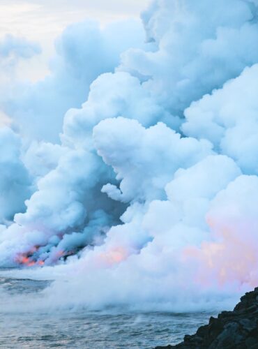 fire and smoke on body of water near rock formation under cloudy sky